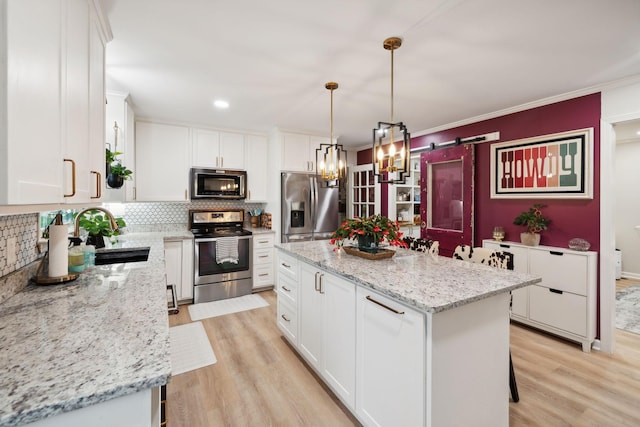 kitchen featuring decorative light fixtures, white cabinetry, sink, a center island, and stainless steel appliances