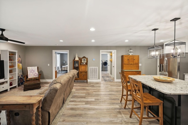 living room with washer / dryer, ceiling fan, and light hardwood / wood-style flooring