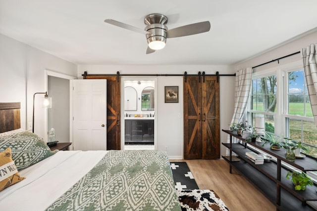 bedroom featuring ensuite bathroom, a barn door, sink, and light hardwood / wood-style flooring