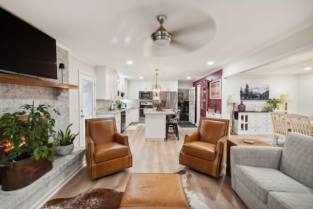 living room featuring a brick fireplace, ornamental molding, ceiling fan, a barn door, and light hardwood / wood-style floors