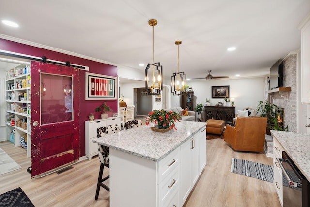 kitchen with white cabinetry, hanging light fixtures, light hardwood / wood-style floors, a kitchen island, and a barn door