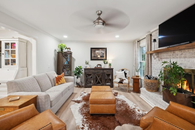 living room with crown molding, a brick fireplace, ceiling fan, and light wood-type flooring