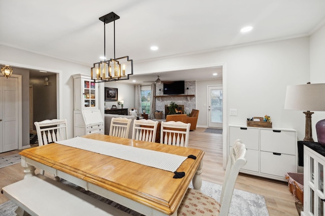 dining area with crown molding, ceiling fan with notable chandelier, a large fireplace, and light wood-type flooring