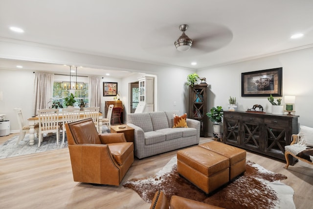 living room featuring ceiling fan with notable chandelier, light hardwood / wood-style flooring, and ornamental molding