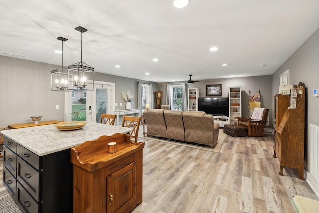 kitchen featuring ceiling fan, hanging light fixtures, light hardwood / wood-style floors, light stone countertops, and a kitchen island