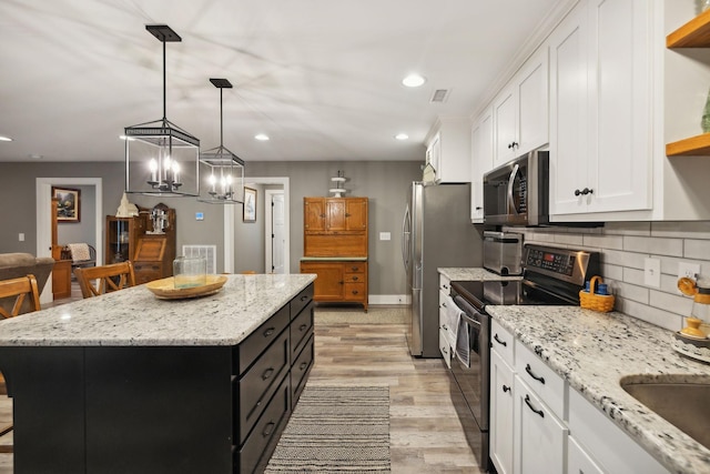 kitchen with a breakfast bar, appliances with stainless steel finishes, white cabinets, a kitchen island, and decorative light fixtures