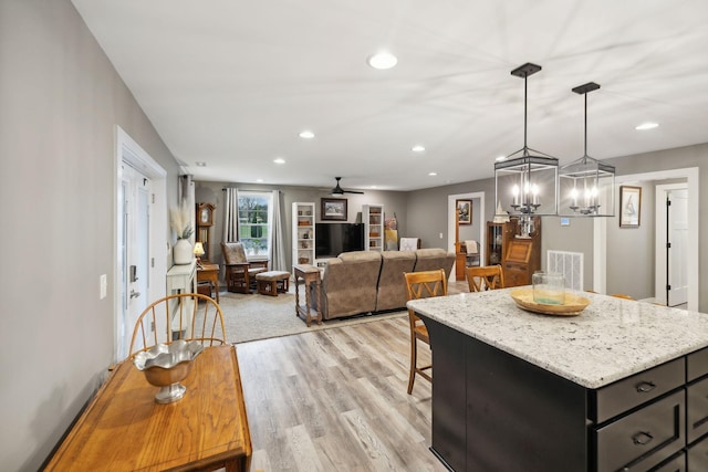 kitchen with a kitchen island, ceiling fan with notable chandelier, pendant lighting, light stone counters, and light hardwood / wood-style floors