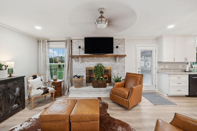 living room with crown molding, ceiling fan, a brick fireplace, and light wood-type flooring