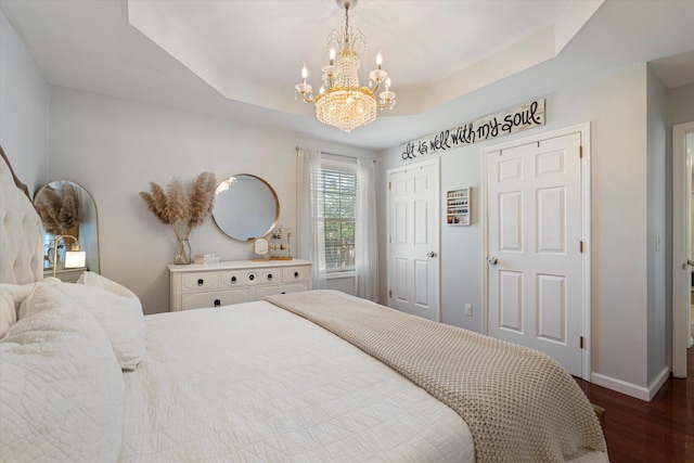 bedroom with a notable chandelier, a tray ceiling, dark hardwood / wood-style floors, and multiple closets