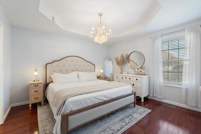 bedroom with dark wood-type flooring, a raised ceiling, and a chandelier