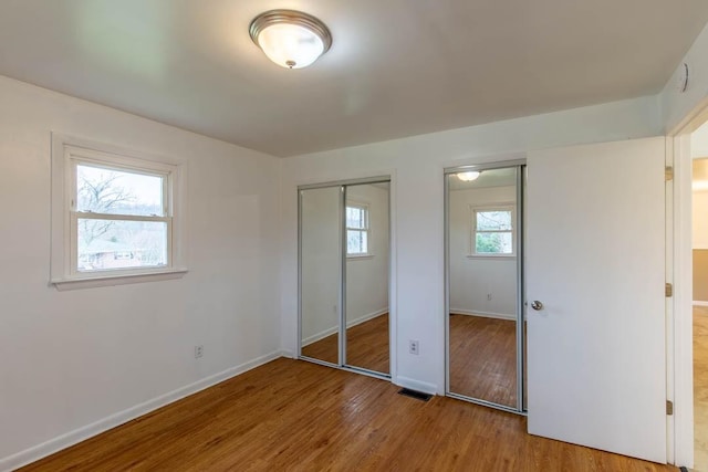 unfurnished bedroom featuring wood-type flooring and two closets