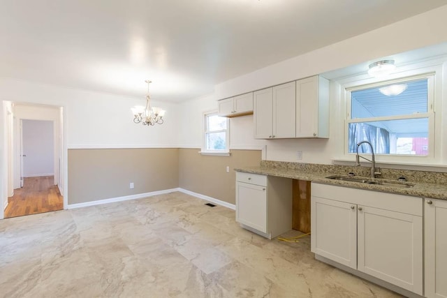 kitchen featuring pendant lighting, sink, white cabinetry, an inviting chandelier, and light stone counters