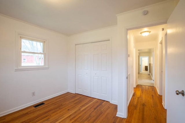 unfurnished bedroom with hardwood / wood-style floors, crown molding, and a closet