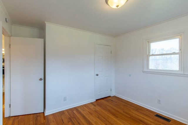 unfurnished bedroom featuring hardwood / wood-style flooring, ornamental molding, and a closet