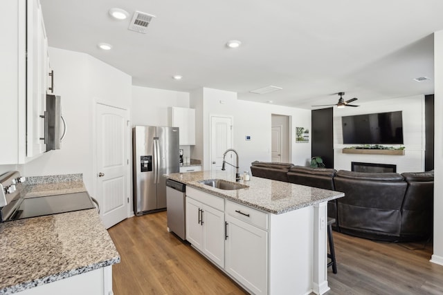 kitchen featuring appliances with stainless steel finishes, white cabinetry, wood-type flooring, sink, and a center island with sink