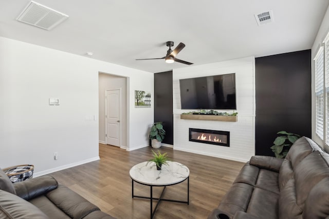 living room featuring wood-type flooring, ceiling fan, and a fireplace