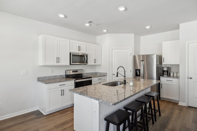 kitchen featuring appliances with stainless steel finishes, an island with sink, sink, white cabinets, and light stone countertops