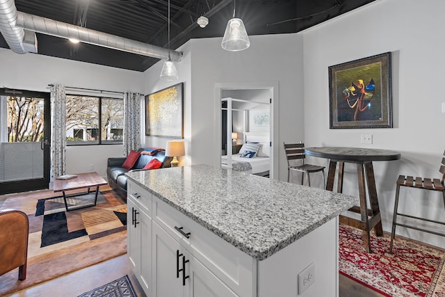 kitchen with a center island, white cabinets, light stone counters, and decorative light fixtures