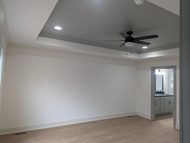 empty room with sink, a raised ceiling, ceiling fan, and light wood-type flooring