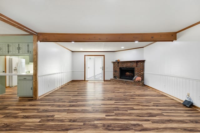 unfurnished living room featuring a brick fireplace, dark wood-type flooring, ornamental molding, and beamed ceiling