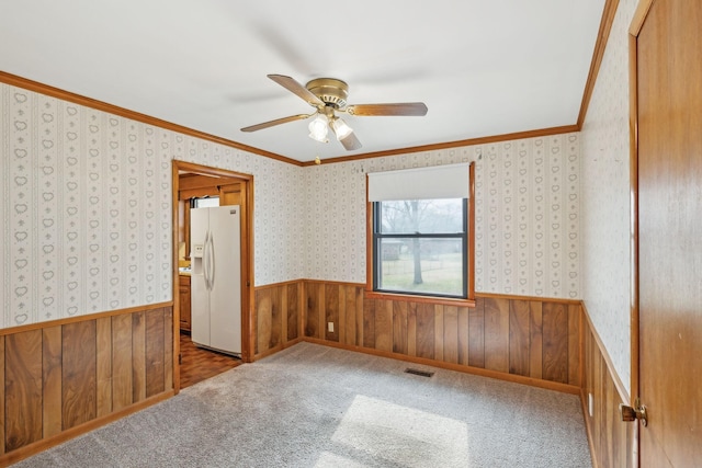 unfurnished bedroom featuring wooden walls, carpet floors, ornamental molding, white fridge with ice dispenser, and ceiling fan