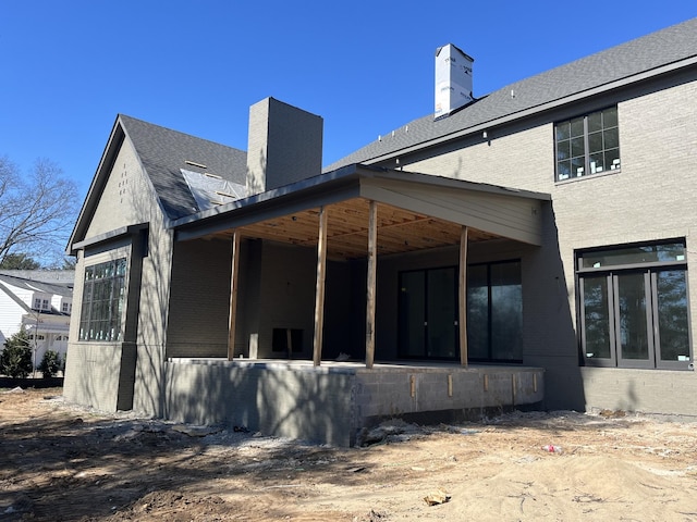 rear view of property featuring a shingled roof and a chimney