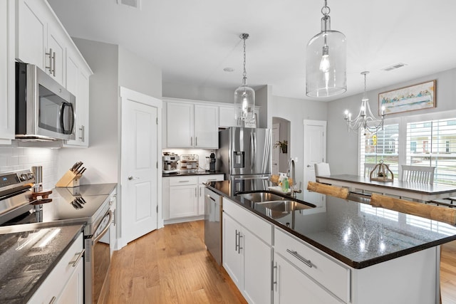 kitchen with appliances with stainless steel finishes, decorative light fixtures, a kitchen island with sink, and sink