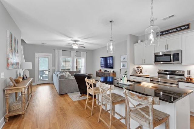 kitchen featuring a breakfast bar area, white cabinetry, decorative light fixtures, stainless steel appliances, and backsplash