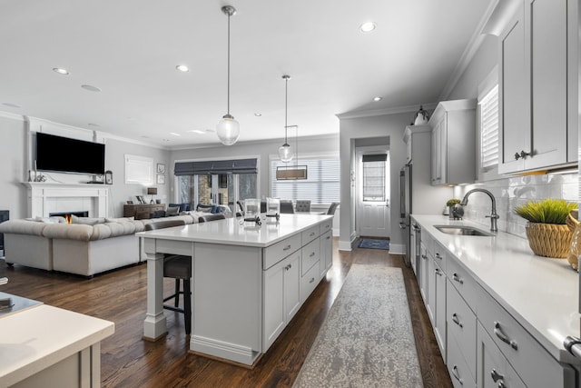 kitchen with decorative light fixtures, an island with sink, sink, decorative backsplash, and dark wood-type flooring