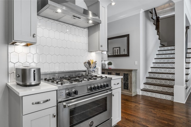 kitchen with wall chimney exhaust hood, white cabinetry, high end stove, dark hardwood / wood-style floors, and decorative backsplash