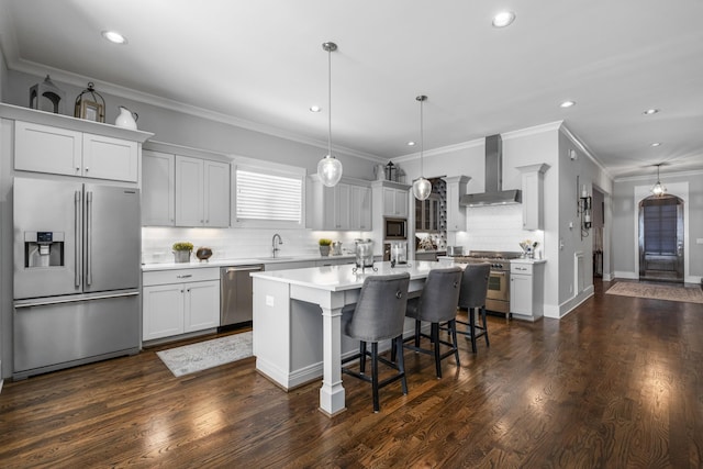 kitchen with appliances with stainless steel finishes, hanging light fixtures, a center island, decorative backsplash, and wall chimney exhaust hood