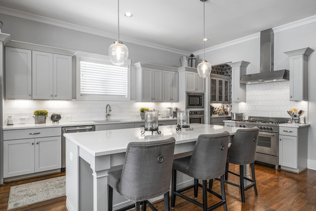 kitchen featuring an island with sink, appliances with stainless steel finishes, sink, and wall chimney range hood