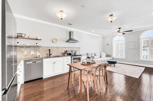 kitchen featuring white cabinetry, backsplash, stainless steel appliances, light stone countertops, and wall chimney exhaust hood