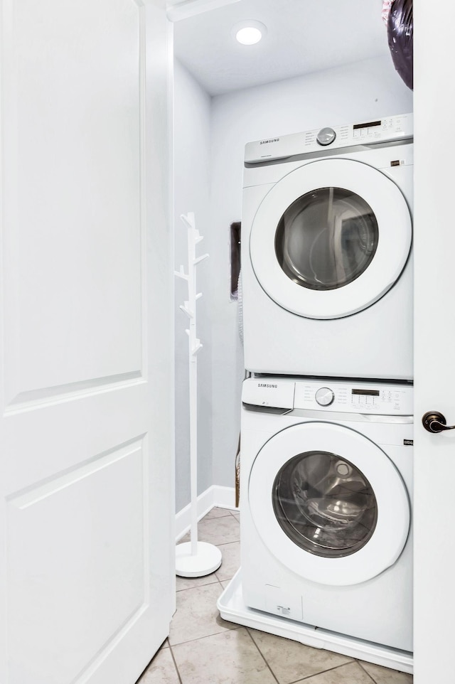 laundry area with stacked washer / drying machine and light tile patterned floors