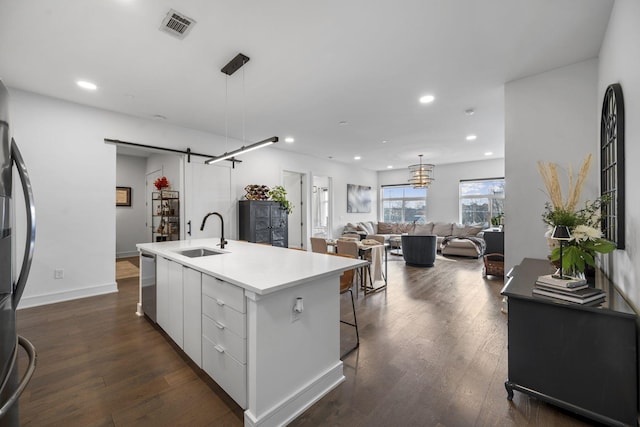 kitchen featuring white cabinetry, a barn door, sink, and a center island with sink