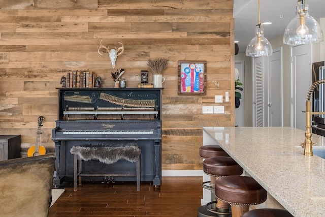 interior space with a breakfast bar area, wood walls, light stone counters, hanging light fixtures, and dark hardwood / wood-style flooring