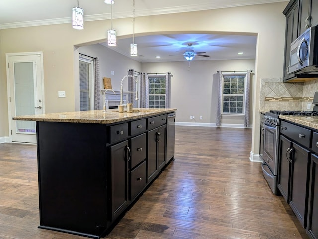 kitchen with a kitchen island with sink, stainless steel appliances, light stone countertops, dark hardwood / wood-style flooring, and decorative light fixtures