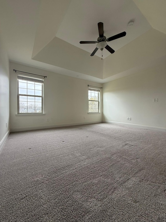 carpeted empty room featuring ceiling fan and a raised ceiling