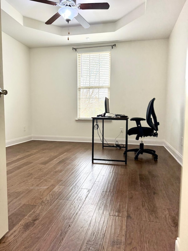 office area with a raised ceiling, dark wood-type flooring, and ceiling fan