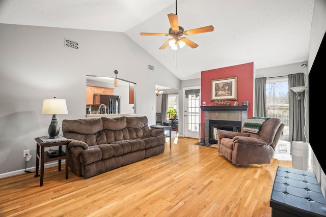 living room featuring a tiled fireplace, wood-type flooring, vaulted ceiling, and plenty of natural light