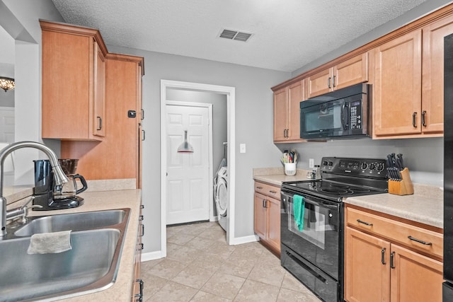 kitchen featuring sink, a textured ceiling, light tile patterned floors, washer / clothes dryer, and black appliances