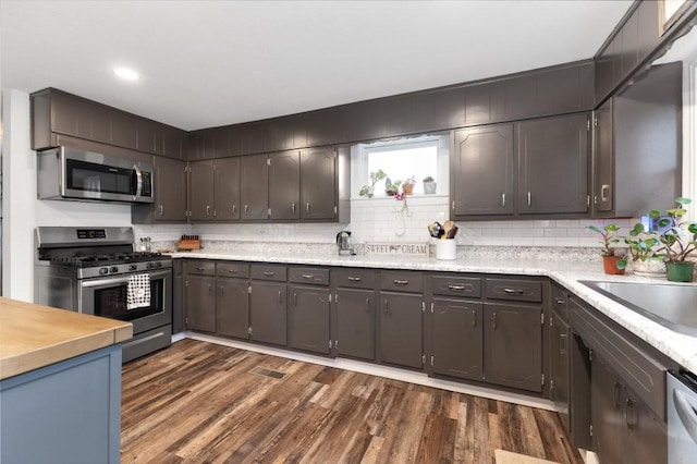 kitchen with sink, stainless steel appliances, dark hardwood / wood-style floors, dark brown cabinetry, and tasteful backsplash