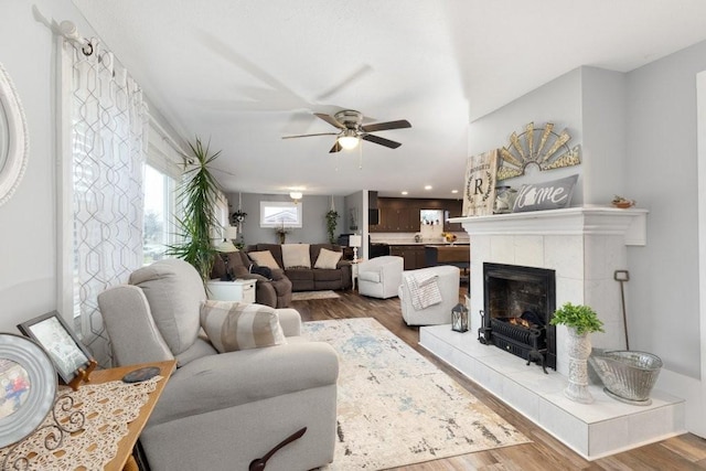 living room with a tiled fireplace, wood-type flooring, and ceiling fan