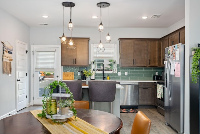 kitchen with a healthy amount of sunlight, appliances with stainless steel finishes, decorative light fixtures, and dark brown cabinetry