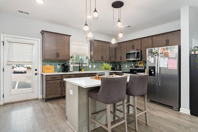 kitchen with dark brown cabinetry, stainless steel appliances, decorative light fixtures, and a kitchen breakfast bar