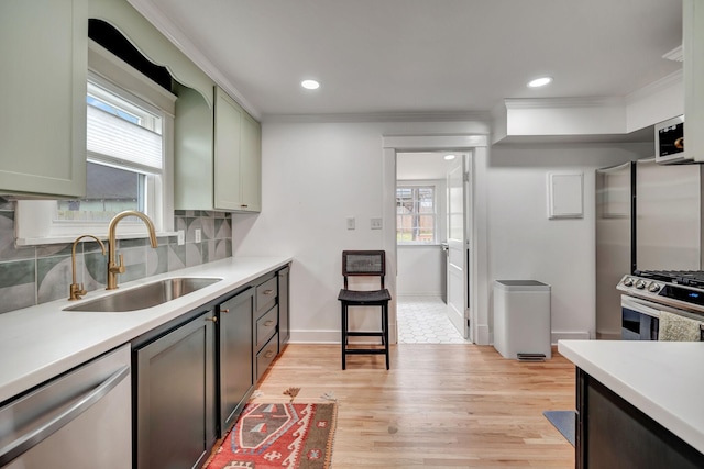 kitchen featuring sink, green cabinetry, appliances with stainless steel finishes, light hardwood / wood-style floors, and decorative backsplash