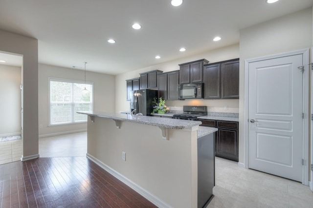 kitchen with hardwood / wood-style flooring, a breakfast bar, a kitchen island with sink, hanging light fixtures, and black appliances