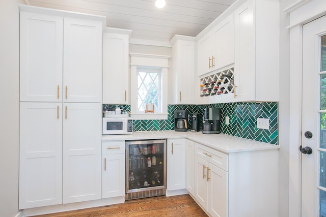 bar featuring wine cooler, backsplash, hardwood / wood-style flooring, and white cabinets