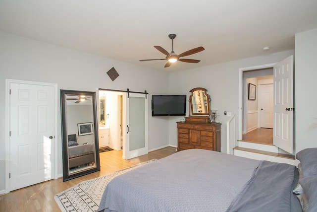 bedroom with ceiling fan, a barn door, connected bathroom, and light hardwood / wood-style floors