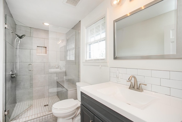 bathroom featuring vanity, toilet, a shower with shower door, and decorative backsplash